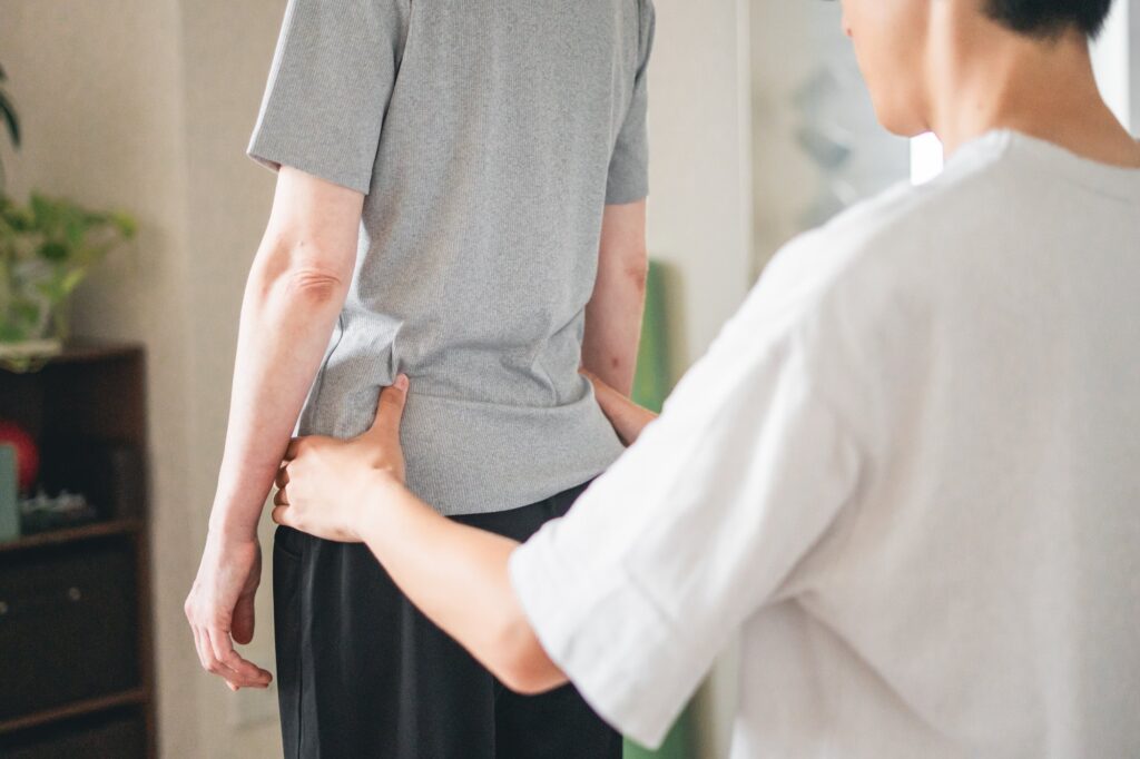 立った姿勢で、骨盤に手を当てて腰まわりを確認している様子